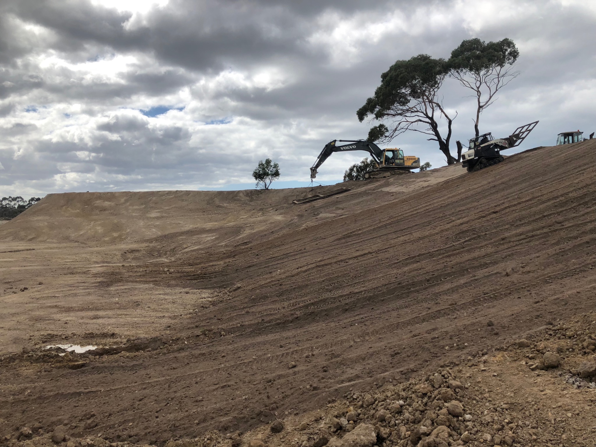 Excavator working along the top of a shaped dirt slope