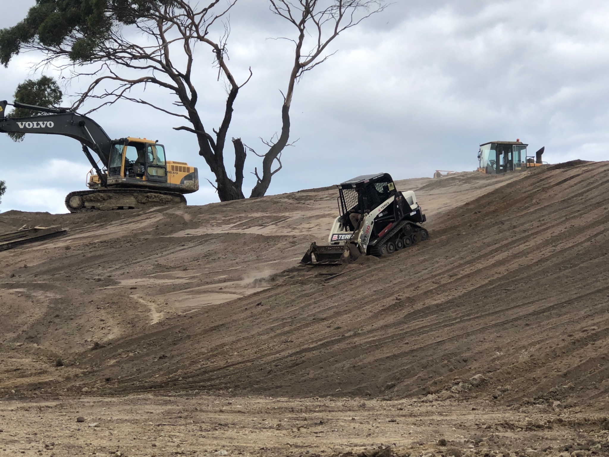 Compact loader working on the bank below an excavator